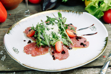  Restaurant dish on a wooden background with vegetables. Salad with beef tenderloin and arugula on a plate.