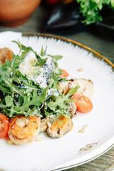  Restaurant dish on a wooden background with vegetables. Salad with shrimp, avocado and arugula on a plate.
