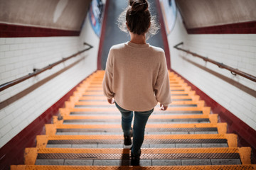 Young woman dressed in a light sweater, jeans and tied hair walking down the stairs leading to the...