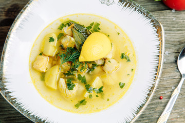 Restaurant dish on a wooden background with vegetables. Soup with fish and seafood and lemon on a plate.