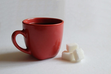 coffee in a red Cup or mug next to three pieces of sugar on a white background with a place to...