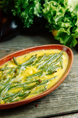 Azerbaijani restaurant dish on a wooden background with vegetables. String beans with raw egg on a clay plate.