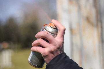 Spray paint close up. Spray paint in hand on outdoors. Orange spray paint can close up
