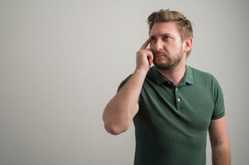 Portrait of serious stylish attractive man with thick beard, dressed in casual green t shirt making thinking gesture