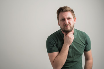 Obraz premium Portrait of serious stylish attractive man with thick beard, dressed in casual green t shirt gesturing neck ache