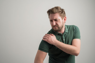 Portrait of serious stylish attractive man with thick beard, dressed in casual green t shirt gesturing shoulder ache