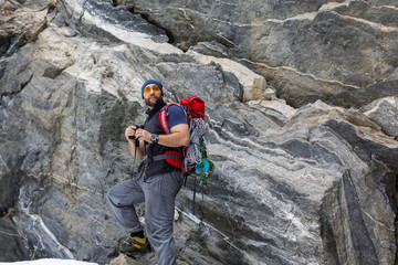 A man tourist with a backpack stands near a sheer stone rock.