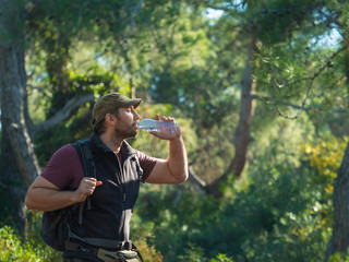 Male tourist drinks clear water from a bottle in the forest.