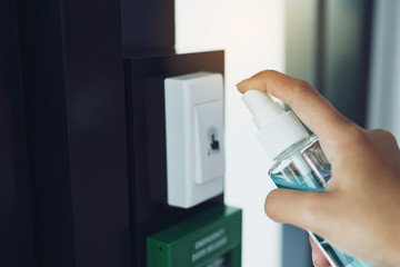 Woman hand spraying alcohol sanitizer bottle to the button control of the door, against Novel coronavirus or Corona Virus Disease (Covid-19) at public indoor