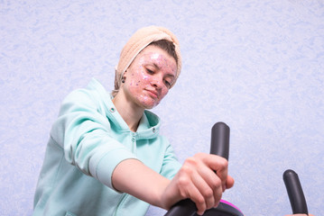 Young attractive woman with moisturizing and cleansing pink mask practices on a stationary bike at home during quarantine