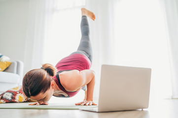 Fototapeta na wymiar Fit sporty healthy woman on mat in Four-Limbed Staff Eka Pada Chaturanga Dandasana pose, doing breathing exercises, watching online yoga class on laptop computer. Healthy . and active people concept.