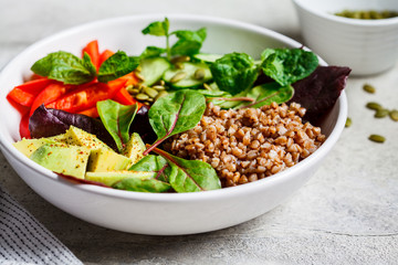 Buddha bowl salad with buckwheat, vegetables and seeds in white plate.