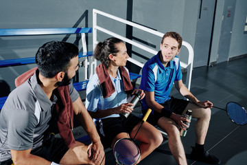 Badminton players resting on bench, drinking water and discussing strategy after game