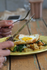 One fried egg and potatoes with fork and knife on yellow plate.