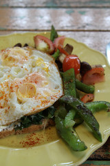 Breakfast, fried eggs, tomatoes, bell pepper, vegetables and bread on yellow plate.
