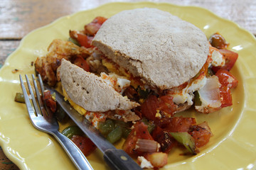 Breakfast, fried eggs, tomatoes, bell pepper, vegetables and bread on yellow plate.