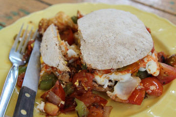 Breakfast, fried eggs, tomatoes, bell pepper, vegetables and bread on yellow plate.