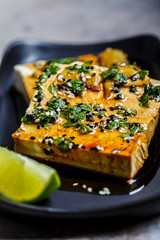 Tofu with marinade of soy sauce, ginger, spices and sesame seeds in black plate.