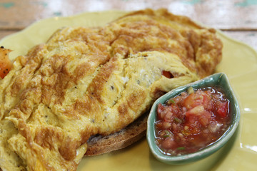 Breakfast; omelet, bread and tomato salad on the side on yellow plate.