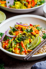 Vegan curry with broccoli, pepper, green beans and brown rice in white bowl.