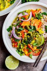 Green thai curry with broccoli, pepper, green beans and brown rice in white bowl, top view.
