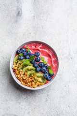 Pink berry smoothie bowl with granola, kiwi and blueberries, light background, top view.