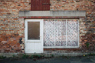 Alte Tür und Schaufenster mit Gardine in einem Backsteinhaus
