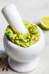 Cooking guacamole - avocado sauce in a white stone mortar.
