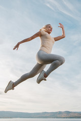 beautiful woman fitness instructor jumps on the sky background