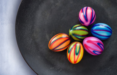 farbig bemalte Ostereier liegen auf einer schwarzen Schale