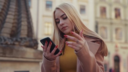 Frustrated blonde woman reads a surprising negative news sms on smartphone social media puts hands down giving up getting upset outside on the street. Bad day concept.