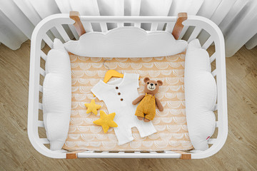 Baby romper with toy bear for a newborn in cot, cradle.  White wooden baby crib with pillows shaped...