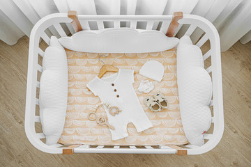 The top view of baby clothes and accessories in cot, cradle. Wooden cradle for newborn with white...