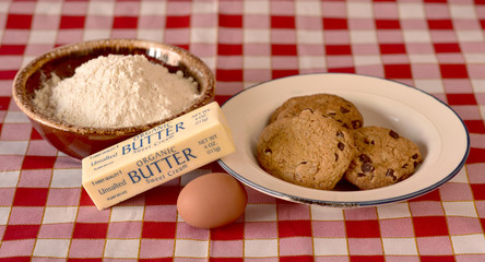 Chocolate Chip Cookies, Butter, an Egg, and Pastry Flour on a Checkered Table Cloth