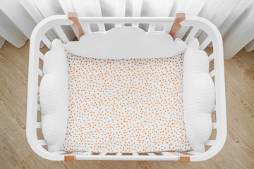 Obraz na płótnie Canvas White wooden baby crib with pillows shaped clouds in baby's room. Top view of child's bed