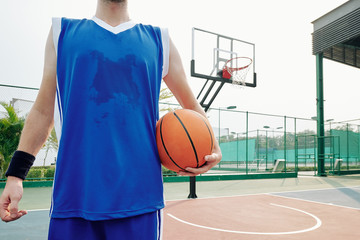 Cropped image of sweaty basketball player standing on outdoor court with ball
