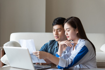 A young asian couple is sitting on a carpet using a computer