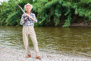 Fototapeta na wymiar Mature fisherman with rod at riverside