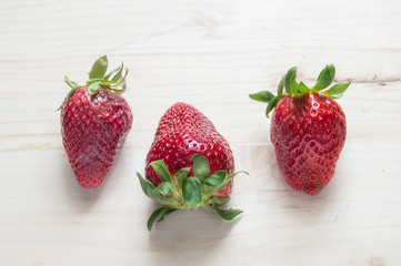 three straeberries isolatedon wooden backgreound