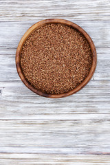 Raw roasted buckwheats in round wooden bowl on light wood. Russian grechka. Organic healthy diet food. Vertical format image with copy space.