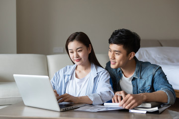 Obraz premium A young asian couple is sitting on a carpet using a computer