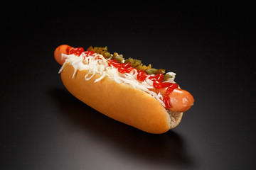 Hot dog with sauerkraut, cream cheese, jalapenos and tomato sauce on a black background.