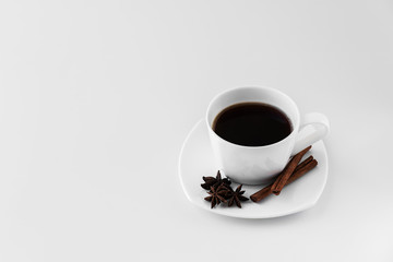 White cup with coffee and saucer, with three star anise star anise and cinnamon sticks, on a white background. A good idea for the menu or sign of a restaurant or cafe, cafeteria