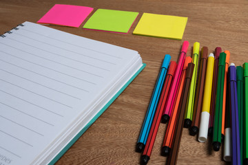 Fototapeta na wymiar cuaderno sobre escritorio acompañado de lapiceros, marcadores con espacio en blanco para poner texto