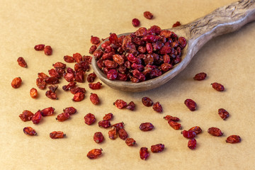 Dried barberry in ceramic spoon on brown paper tablecloth.