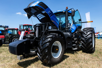 Obraz premium big blue tractor with big wheels in a field in summer at an agricultural exhibition