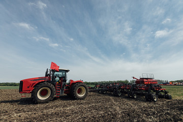 Obraz premium general plan of a red tractor with large wheels and a plow in the field in summer