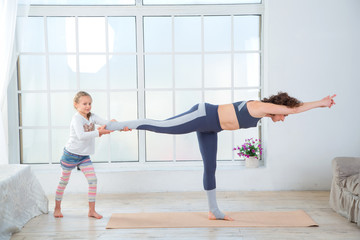 Fitness adult woman with her child. Morning exercises, yoga - do at home all together. Grandmother and granddaughter doing yoga exercise home. Mother and daughter do gymnastics exercises.