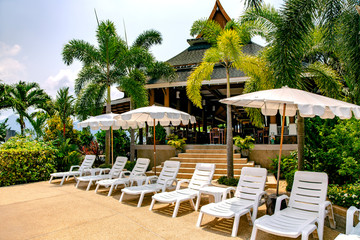 White plastic sun loungers with umbrellas by the pool amidst tropical gardens on Koh Chang island, Thailand