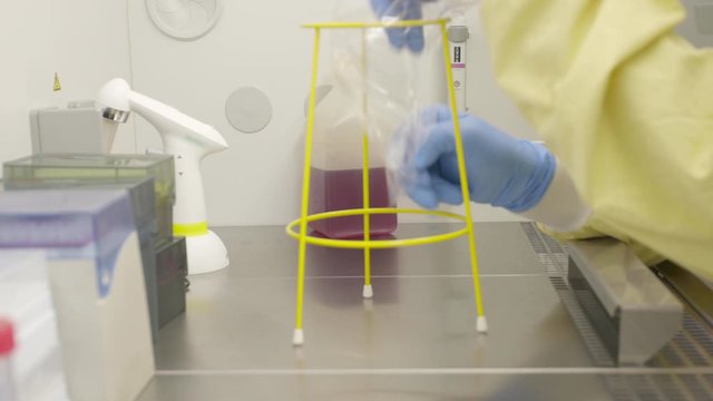 Scientist with laboratory coat and protective gloves putting waste bag in holder under the working bench.